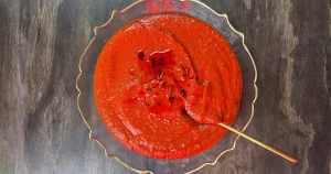 A bowl of Vampire's Red Pepper and Tomato Soup, Drizzled with chili oil and chili flakes