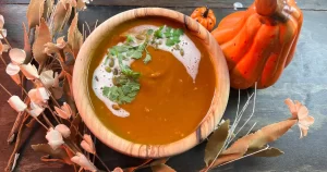 Pumpkin curry in a bowl surrounded by wheat and a pumpkin