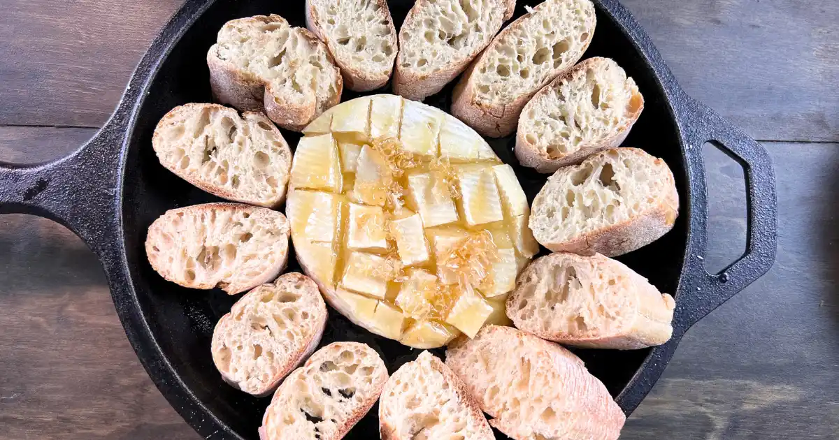 Baked Honey and Butter Cheese Wheel in a cast iron pan, surrounded by baguette slices