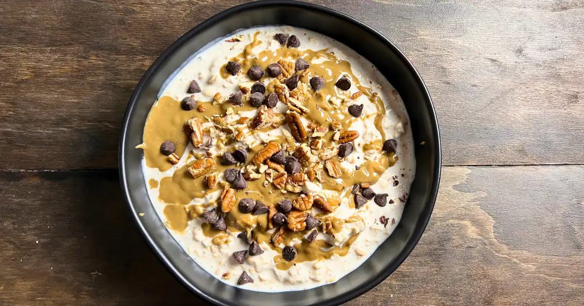 Overnight oats in a bowl topped with sunflower butter, pecans, and chocolate chips