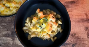 Macaroni and cheese in a bowl, topped with a sprig of oregano